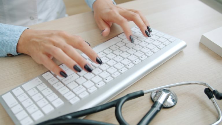 Doctor typing on keyboard with stethoscope nearby